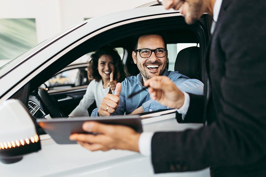 Dealership associate shaking hands with a customer in his new car